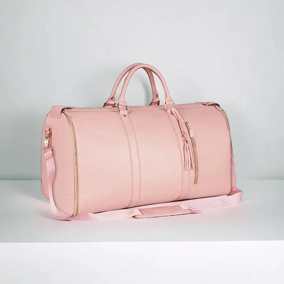 Rosa reisebag med gyldne detaljer og en skulderstropp vises stående på en hvit flate, med en minimalistisk bakgrunn.